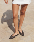 Person wearing black woven flats on a stone pavement