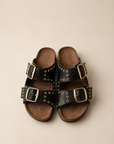 Pair of black sandals with gold buckles on a beige background