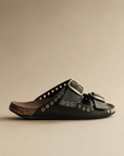 Black leather sandal with gold accents on a beige background
