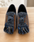 A pair of slip-on loafers with woven brown side panels, blue and white patterned uppers, and long fringe tassels, displayed on a light wood surface.