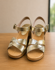 Gold sandals with wooden soles on a wooden surface