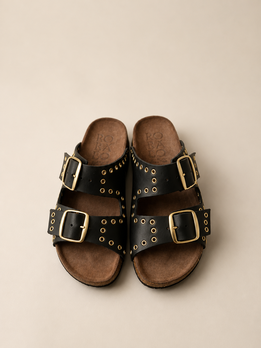 Pair of black sandals with gold buckles on a beige background