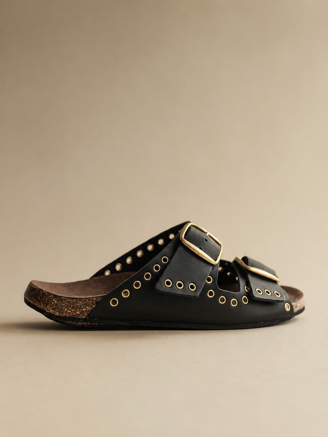 Black leather sandal with gold accents on a beige background