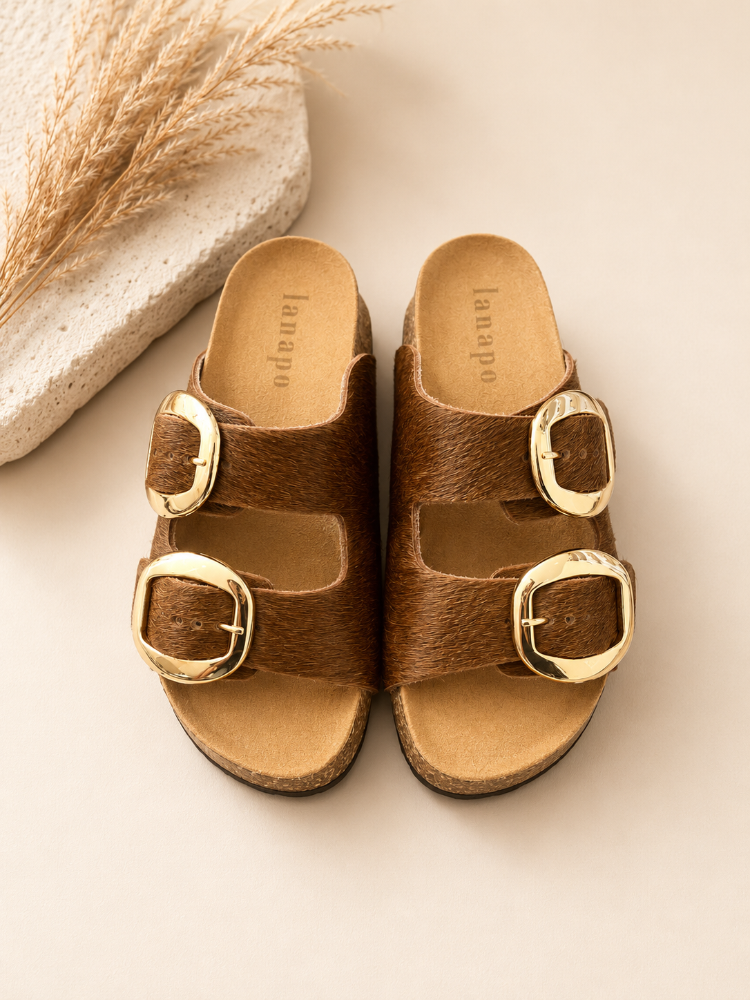 Pair of brown sandals with gold buckles on a light background