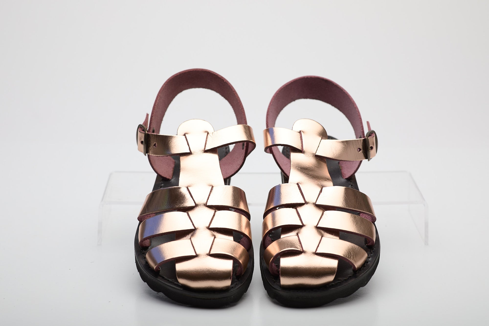 Pair of rose gold sandals on a white background