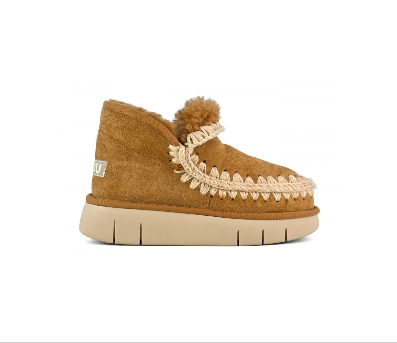A single tan suede moccasin-style slipper with a cream braided trim, fluffy pom-pom, and thick cream sole, shown in profile against a white background.